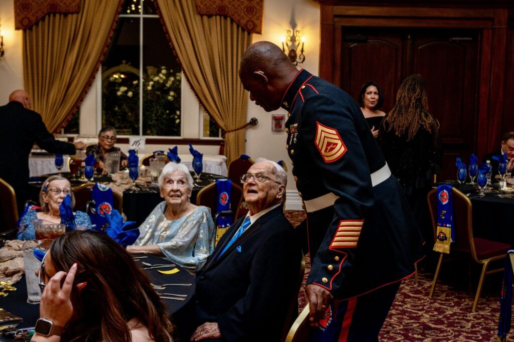 Marine in dress blues greeting a senior veteran at his table at the 2025 Military Ball